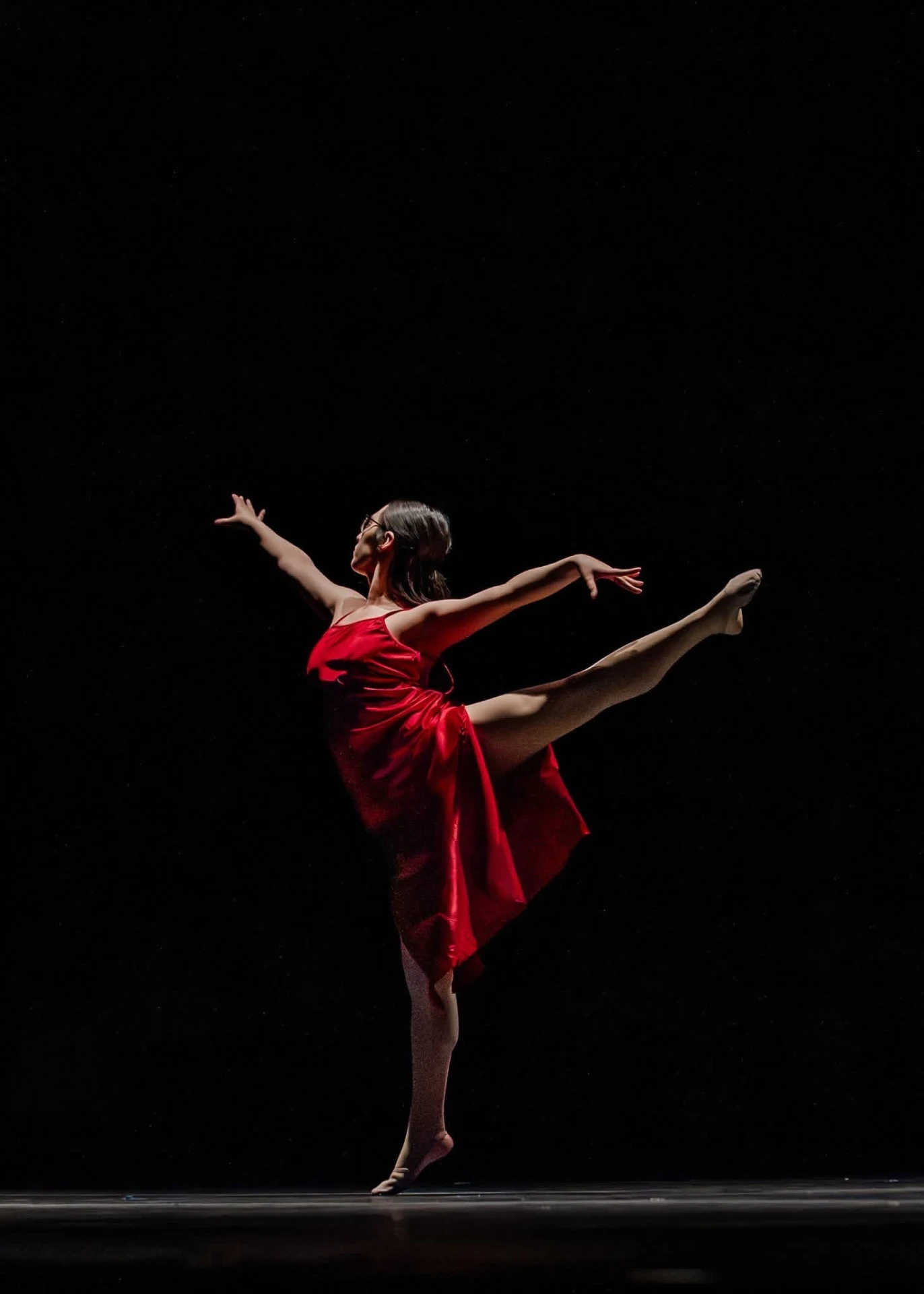 Forever Elite dancer in a red dress holding an arabesque on a darkened stage